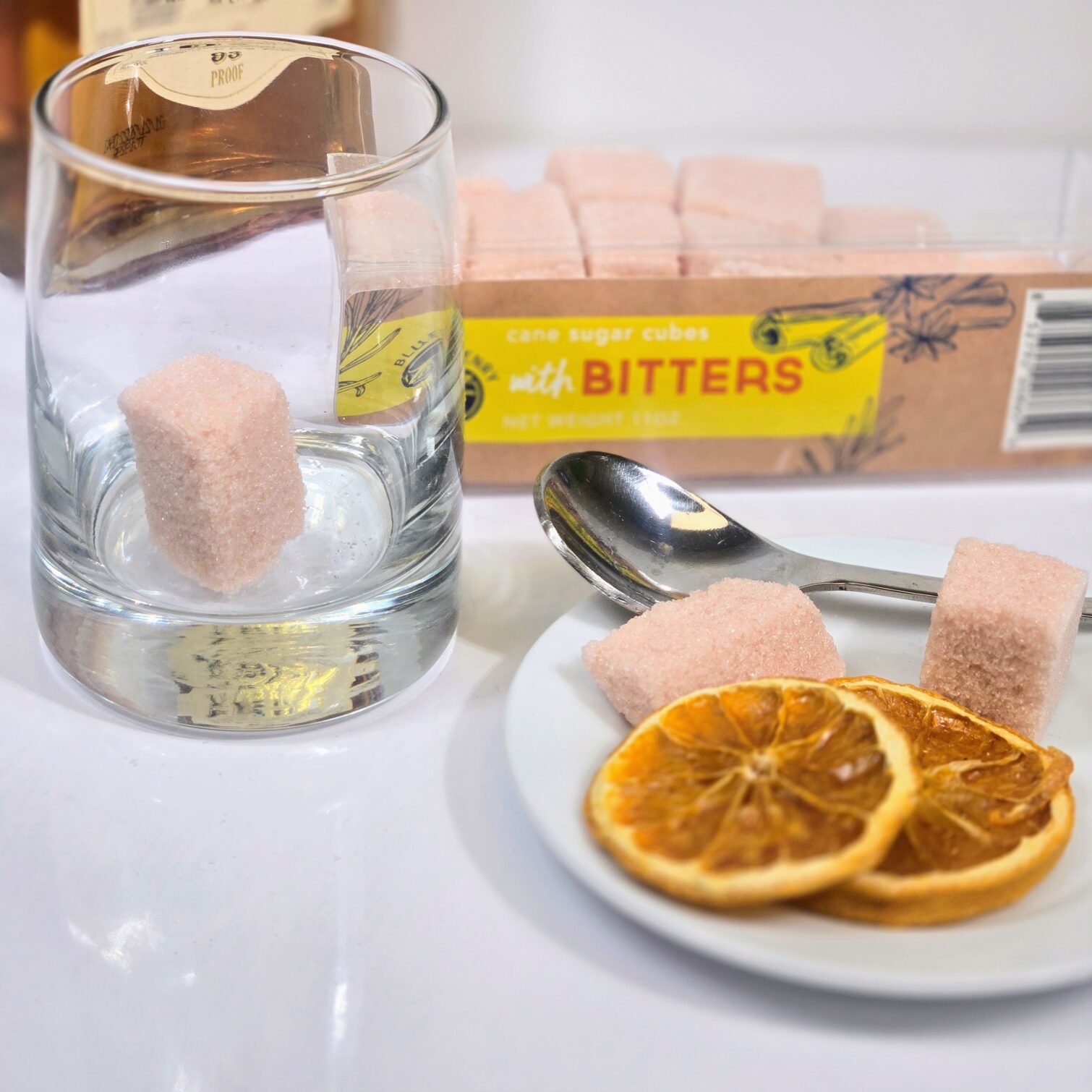 Box of BlueHenry Cane Sugar Cubes infused with Bitters accompanied with Dehydrated Orange slices and Whiskey to make an Old-Fashioned cocktail in a lowball glass