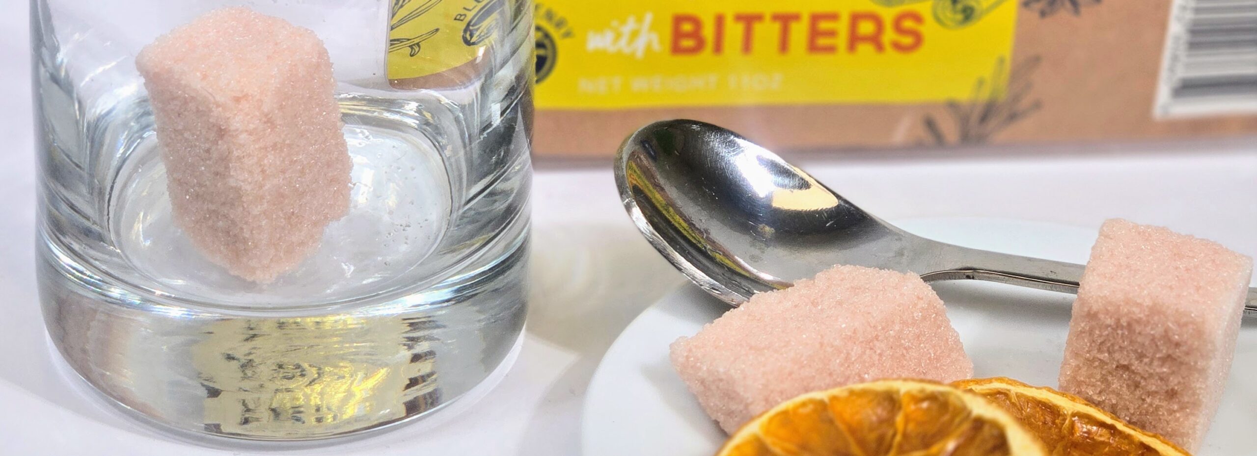 Box of BlueHenry Cane Sugar Cubes infused with Bitters accompanied with Dehydrated Orange slices and Whiskey to make an Old-Fashioned cocktail in a lowball glass