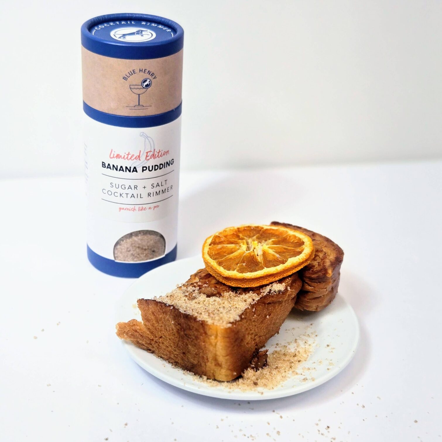 Tube of BlueHenry Limited Edition Banana Pudding Glass Rimming Sugar/Salt next to a decadent slice of thick toast that has the banana pudding sugar/salt sprinkled on top with a slice of BlueHenry dehydrated orange.