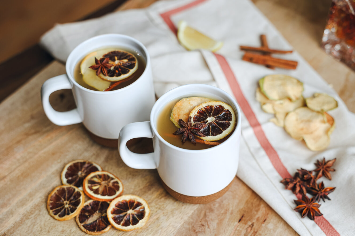 Two cups of tea garnished with BlueHenry lemon and apple slices along with star anise and cinnamon sticks